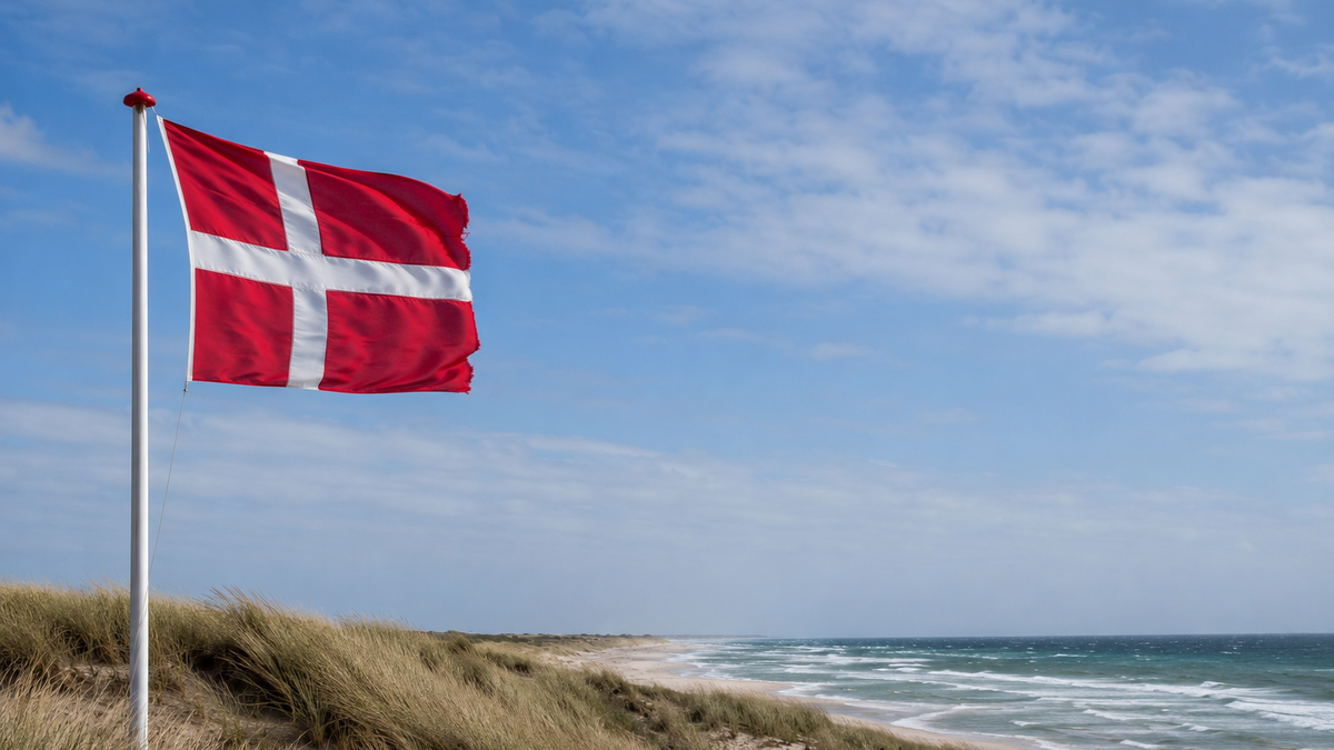 A Danish flag flying beside coastal dunes and the sea